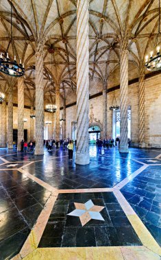 İnsanlar Valencia İspanya 'da Lonja de la Seda' yı keşfediyorlar. Tarihi binada uzun sütunlar ve karmaşık katlar yer alıyor. Ziyaretçiler mimariye hayran..