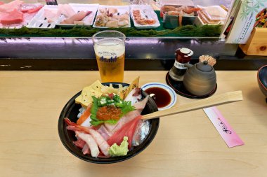 Shibuya, Tokyo 'da bir suşi barında bir kase sashimi bir masada oturur. Arkasında, çeşitli suşi seçenekleri gösteriliyor.
