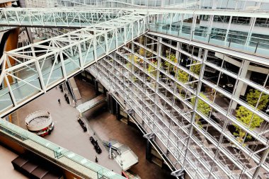 İnsanlar Tokyo 'daki Uluslararası Forum' dan geçiyor. Yapıda cam duvarlar ve açık alanlar var. Bölgede ağaçlar görülebilir..