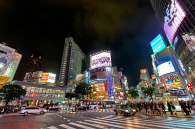 Tokyo 'nun Shibuya ilçesi geceleri parlak ışıklar, hareket eden arabalar ve yürüyen insanlarla dolu sokaklar gösteriyor. Canlı bir atmosfer var..