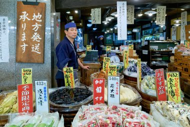 Japonya 'nın Kyoto kentindeki Nishiki Market' te bir satıcı çeşitli gıda ürünleri arasında yer alıyor. Müşteriler satılık ürünlerin renkli görüntülerine göz atıyorlar.