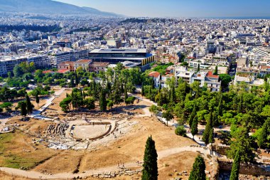 Akropolis manzarası, Atina şehir planlarını ve antik Dionysus tiyatrosunu gün ışığında ağaçlar ve binalar arasında gösteriyor.