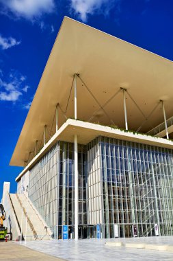 Ziyaretçiler Atina 'daki Stavros Niarchos Vakfı Kültür Merkezi yakınlarında yürüyorlar. Güneş eşsiz bina tasarımı ve yapısı üzerinde parlıyor..