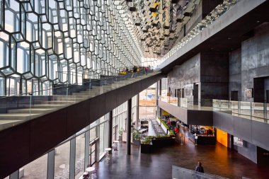İnsanlar güneşli bir günde Reykjavik, İzlanda 'daki Harpa konser salonunda yürüyüp etkileşime geçiyorlar. Binanın tasarımı göze çarpıyor..