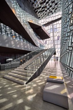 Reykjavik 'teki Harpa konser salonunun merdivenlerinden iki kişi geçiyor. Güneş ışığı yerde ve duvarlarda desenler oluşturur..