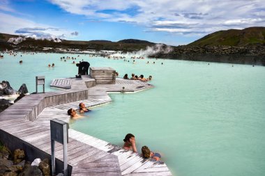 Ziyaretçiler İzlanda 'daki Blue Lagoon Spa' nın ılık sularının tadını çıkarıyorlar. İnsanlar doğayla çevrili jeotermal havuzda rahatlar ve sosyalleşirler..