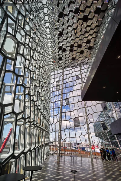 Ziyaretçiler Reykjavik 'teki Harpa konser salonuna parlak bir gökyüzünün altında bakıyorlar. Pencerelerin ve duvarların eşsiz tasarımı ilginç gölgeler yaratır..