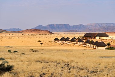 Ziyaretçiler Namib Naukluft Ulusal Parkı 'nda, Namibya' nın akşam ışığında çöl ve dağlarla çevrili basit pansiyonlarda kalıyorlar..