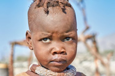 Namibya 'nın Kunene bölgesindeki Himba köyünde bir çocuk, geleneksel mücevherleri takıp kameraya tuhaf bir şekilde bakıyor..