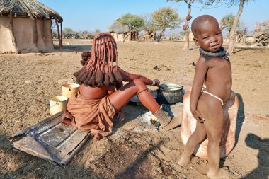 Bir anne ve oğlu, Namibya 'nın Kunene bölgesindeki Himba köyünde günlük aktiviteler ve kültürel yaşamla meşguller..