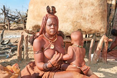 Bir Himba kadını Namibya 'nın Kunene bölgesindeki bir köyde çocuğuna bakıyor, günlük yaşam ve kültürel uygulamalar sergiliyor..