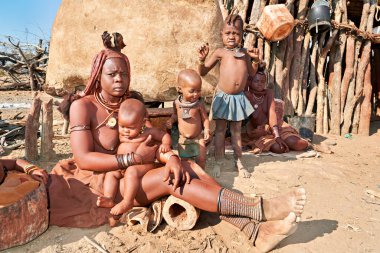 Bir Himba ailesi Kunene Bölgesi, Namibya 'daki evlerinin önünde toplanıyor. Yetişkinler günlük işlerle uğraşırken çocuklar yakınlarda oynuyorlar.