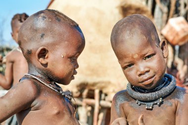 İki çocuk Himba köyünde bir arada duruyor, Namibya 'nın Kunene Bölgesi' ndeki çevrelerini keşfediyor ve gülümsüyor..