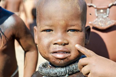 Kunene Bölgesi, Namibya 'da bir köyün önünde Himba' lı bir çocuk duruyor. Çocuk merakla doğrudan kameraya bakıyor..