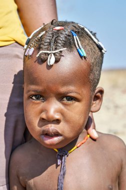 Kunene bölgesinde Zemba Bantu etnik grubundan bir çocuk bulunuyor. Çocuk geleneksel saç modelini gösteriyor ve basit bir kolye takıyor..
