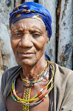 Namibya 'nın Kunene bölgesinde Zemba Bantu etnik grubundan yaşlı bir kadın duruyor. Geleneksel kıyafetler ve mücevherler giyiyor..