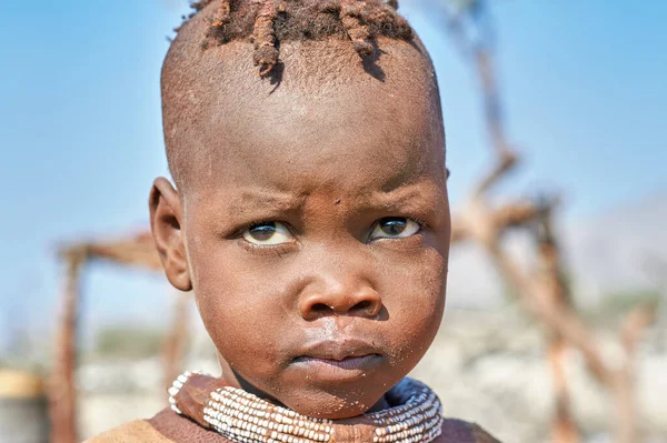 Namibya 'nın Kunene bölgesindeki Himba köyünde bir çocuk, geleneksel mücevherleri takıp kameraya tuhaf bir şekilde bakıyor..