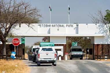 Ziyaretçiler gün boyunca Namibya 'daki Etosha Ulusal Parkı' nın girişine geliyorlar. Araçlar giriş kapısında durur..