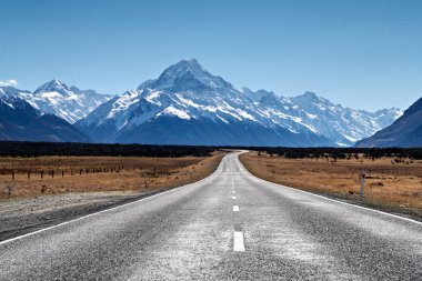 Yeni Zelanda 'daki Aoraki Ulusal Parkı' nda Aoraki Dağı aşçısına doğru uzun bir yol uzanıyor. Dağlar berrak bir gökyüzünün altında yükselir..