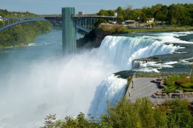 Turistler, arka planda Gökkuşağı Köprüsü ve Gözlem Kulesi ile güçlü Niagara Şelalesi 'ni Amerikan tarafından seyrederek doğal güzelliğin tadını çıkarıyorlar..