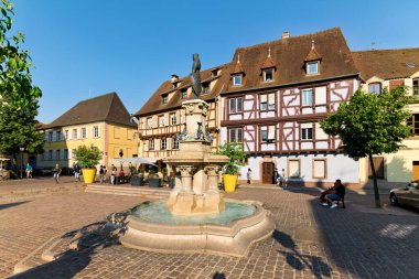 İnsanlar, güneşli bir günde geleneksel ahşap çerçeveli evlere hayran olan Petite Venise, Colmar 'daki Roesselmann çeşmesinin etrafında toplanıyorlar..