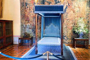 Ziyaretçiler, tarihi dekorlar ve mobilyalarla çevrili Chenonceau Şatosu 'nun yatak odasındaki mavi örtülü yatağı inceliyorlar..