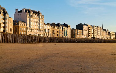 İnsanlar alacakaranlıkta Grand Plage du Sillon boyunca yürür. Güneş binaların arkasında batıyor, kumlara uzun gölgeler bırakıyor..