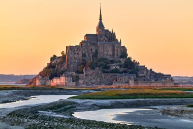 Mont Saint Michel, gün batımında Normandiya 'da dimdik ayakta duruyor. Gökyüzü renk değiştirir ve etrafındaki su ışığı yansıtır..