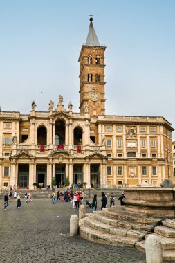 Ziyaretçiler Roma 'daki Aziz Mary Bazilikası' nın önünde toplanıyorlar. Tarihi binalarda mimari detaylar ve yüksek bir çan kulesi sergileniyor..