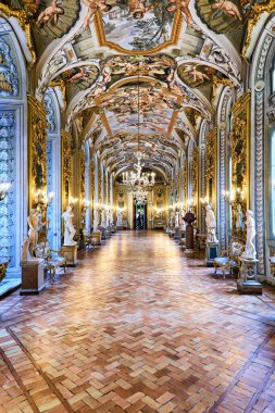 Ziyaretçiler, sergilenen sanat ve heykellere hayran kalarak Roma 'daki Doria Pamphilj Galerisi' nde yürüyorlar. Salonda aynalar ve süslemeler var..