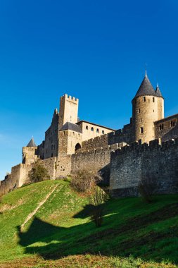 Turistler, Fransa 'daki eski Carcassonne kalesini keşfeder. Açık mavi gökyüzünün altında, eski taş duvarların manzarasının keyfini çıkarırlar..