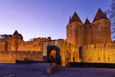 Carcassonne 'un antik duvarları Fransa' da gece çökerken parlıyor. Ziyaretçiler kaleyi geziyor ve bu tarihi mekanda manzaranın tadını çıkarıyorlar..