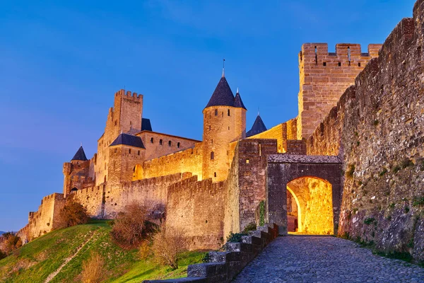 Ziyaretçiler Carcassonne, Fransa 'nın tarihi kale duvarları yakınındaki patikalardan yürür güneş batar ve taşları aydınlatır..