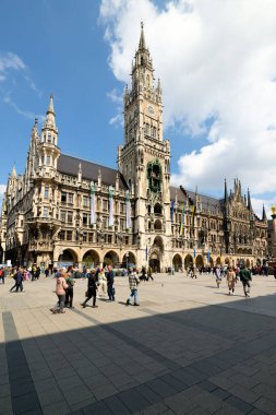 Marienplatz 'da yürüyen insanlar, Almanya' nın Münih kentindeki belediye binasının manzarasının tadını çıkarıyorlar. Bulutlar tarihi meydanda gökyüzünü dolduruyor.