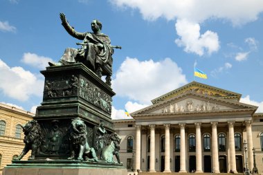 Almanya 'nın Münih kentindeki Marstall Meydanı' ndaki tiyatronun önünde bir heykel duruyor. Güneşli bir günde insanlar çevrede dolaşır..