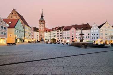 İnsanlar Landsberg am Lech 'teki Hauptplatz Meydanı' nı güneş renkli binaların üzerinde batarken keşfediyorlar. Atmosfer açık dükkanlarla dolu..