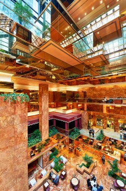 İnsanlar Trump Tower Atrium 'da dolaşırken iç tasarımın ve uzun cam tavanların keyfini çıkarıyorlar. Bitkiler atmosfere eklenir.
