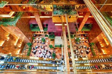 Bazıları merdivenlerde yürürken insanlar Trump Tower Atrium 'da oturup konuşuyorlar. Uzayın birçok bitkisi ve yansıtıcı yüzeyleri vardır..