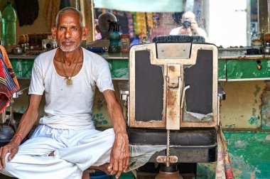 Mandawa, Rajasthan 'daki dükkanında bir berber oturuyor. Mekanı yansıtan aletler ve aynalarla çevrili halde müşterileri bekliyor..
