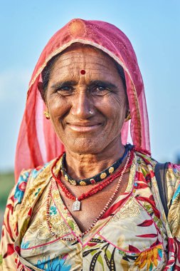 Khimsar, Rajasthan 'da geleneksel kıyafetler ve eşarp takan yaşlı bir kadın gülümsüyor. Açık gökyüzü ile açık havanın tadını çıkarıyor..
