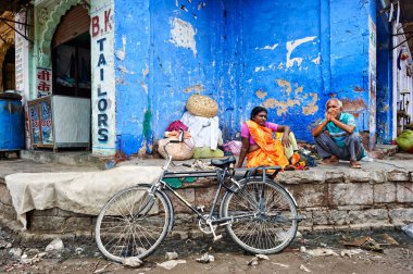 İnsanlar Sardar Market, Jodhpur 'daki dükkanların önünde oturuyor. Civarda günlük hayat devam ederken, yakınlarda bir bisiklet park halinde..