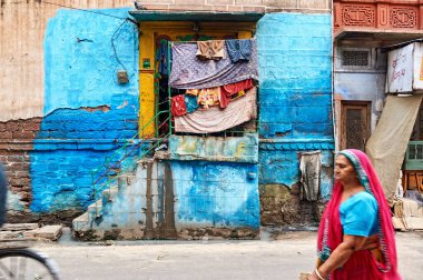 Jodhpur 'da mavi bir duvarın önünden renkli giysiler asılmış bir adam geçiyor. Sokak, şehrin günlük yaşamını ve karakterini gösteriyor..