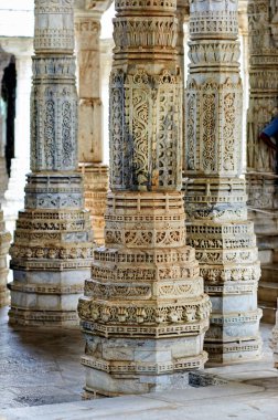 Ziyaretçiler Ranakpur, Rajasthan 'daki eski Jain tapınaklarını keşfediyorlar. Sütunlar ayrıntılı oymalar ve desenler gösteriyor. Güneş ışığı boşluğu doldurur.
