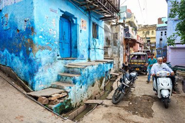 Rajasthan, Bundi 'de süslü boyalı bir ev var. İnsanlar, canlı mavi renkler ve basamaklar içeren binanın yanında yürüyorlar..
