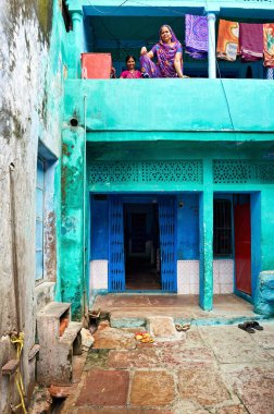 Bundi Rajasthan 'da dekore edilmiş bir evin balkonunda duran iki kadın. Giysiler balkonda asılı. Sokakta taş döşemeler var..