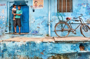 Boyalı mavi bir evde oğlunu tutan bir adam var. Yakınlarda bir bisiklet park edilmiş. Sahne Bundi, Rajasthan 'daki günlük hayatı gösteriyor..