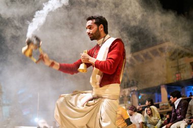 Varanasi 'deki bir nehirde aarti yapan biri. Dindarlar akşam namazında sunaktan dumanlar yükselirken izlerler..