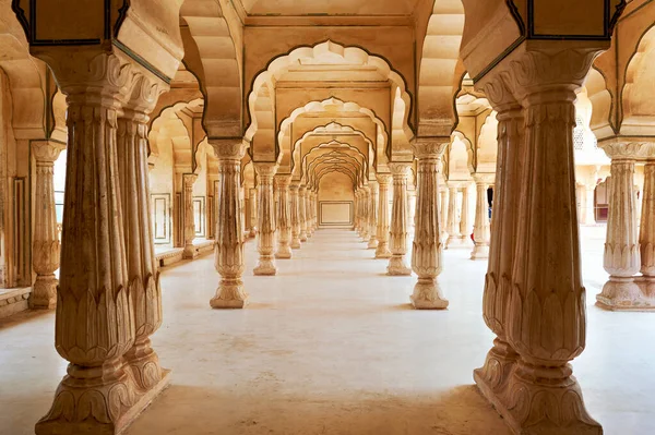 Ziyaretçiler Rajasthan 'daki Amber Sarayı' nda uzun sütunlarla koridorda yürüyorlar. Saray detaylı tasarımlar ve tarihi özellikler sergiliyor..