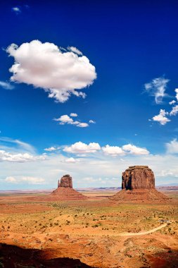 Anıt Vadisi 'nde bulutlu mavi gökyüzü altında yükselen iki büyük kaya oluşumu Navajo halkının eşsiz manzarasını temsil ediyor..