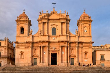 Noto Katedrali İtalya 'nın Noto, Sicilya şehrinde yer almaktadır. Güneş binanın arkasında batıyor, mimarisini vurguluyor. İnsanlar siteyi ziyaret ediyor.